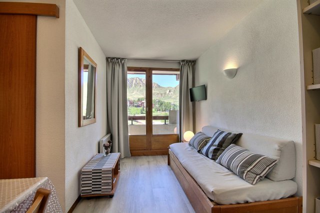 Séjour du studio : banquette-lit et porte-fenêtre ouverte sur la montagne.